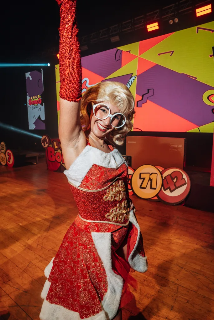 Azafata de Loco Bongo con gafas y traje rojo navideño posando en el escenario