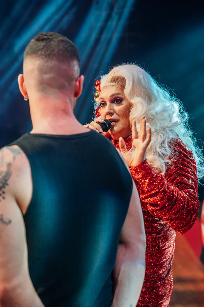 Xenon Spain con micrófono y vestido rojo de lentejuelas junto a un asistente en el escenario de Loco Bongo