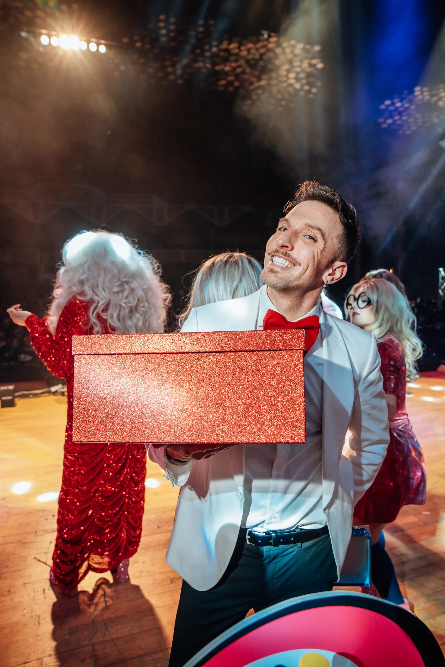 Presentador de Loco Bongo con chaqueta blanca sosteniendo una caja regalo roja en el escenario